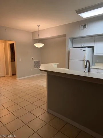 Kitchen with light countertops, refrigerator, decorative light fixtures, light tile patterned floors, and white cabinets