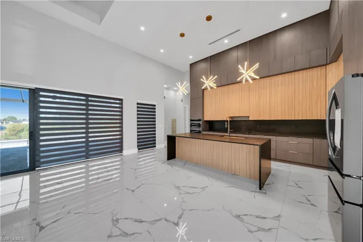 Kitchen featuring dark countertops, modern cabinets, marble finish floor, a high ceiling, and freestanding refrigerator