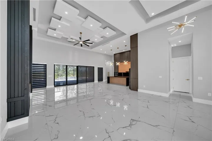 Unfurnished living room featuring baseboards, marble finish floor, recessed lighting, and a tray ceiling