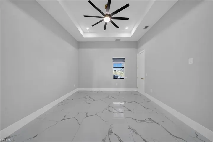 Spare room with a tray ceiling, baseboards, recessed lighting, marble finish floor, and ceiling fan