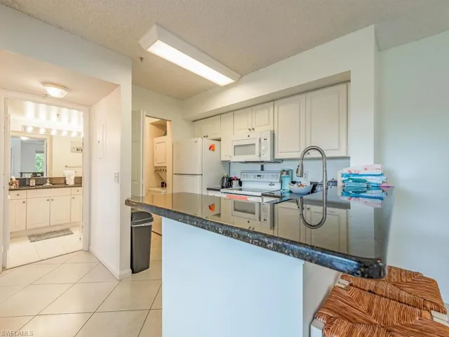 Kitchen featuring white appliances, white cabinets, kitchen peninsula, and light tile floors