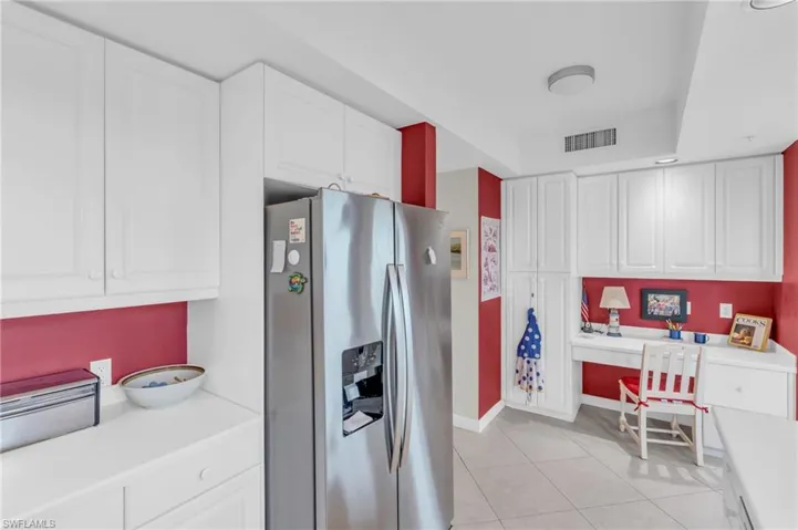 Kitchen featuring white cabinets, stainless steel fridge, built in desk, and light tile patterned flooring