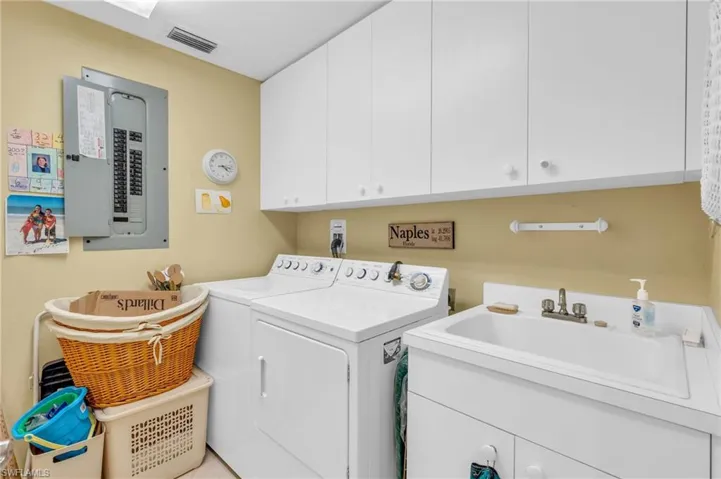 Clothes washing area featuring cabinets, electric panel, washer and clothes dryer, and sink