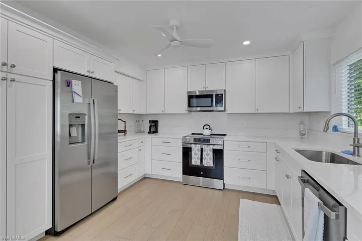 Kitchen with appliances with stainless steel finishes, white cabinetry, light stone counters, a ceiling fan, and recessed lighting