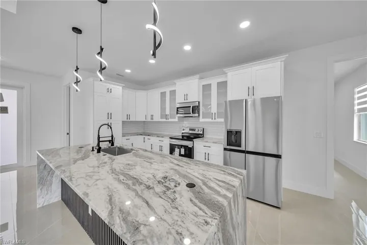 Kitchen with appliances with stainless steel finishes, hanging light fixtures, white cabinets, a large island, and sink