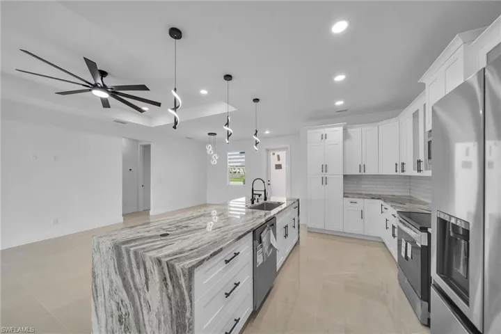 Kitchen featuring ceiling fan, white cabinets, light stone counters, a large island with sink, and appliances with stainless steel finishes
