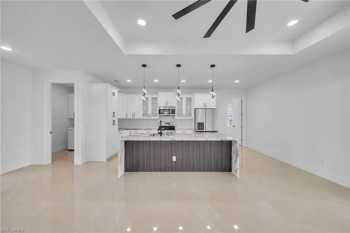 Kitchen with white cabinets, stainless steel appliances, decorative light fixtures, ceiling fan, and a spacious island