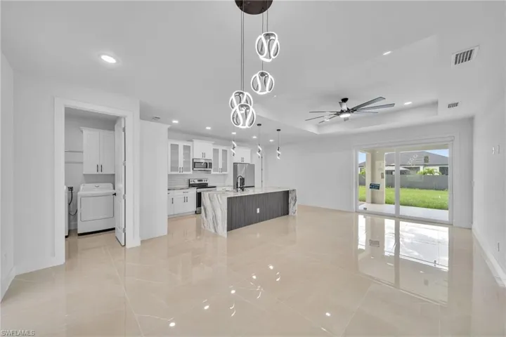 Kitchen with hanging light fixtures, white cabinetry, an island with sink, stainless steel appliances, and ceiling fan