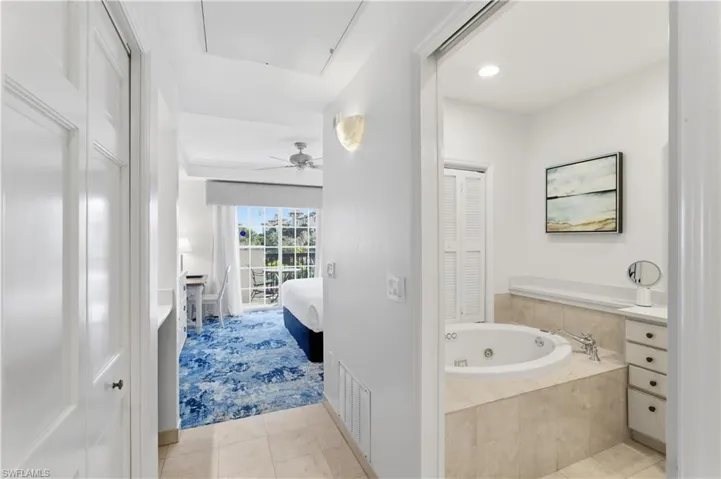 Ensuite bathroom featuring a closet, a ceiling fan, light tile patterned flooring, a jetted tub, and vanity