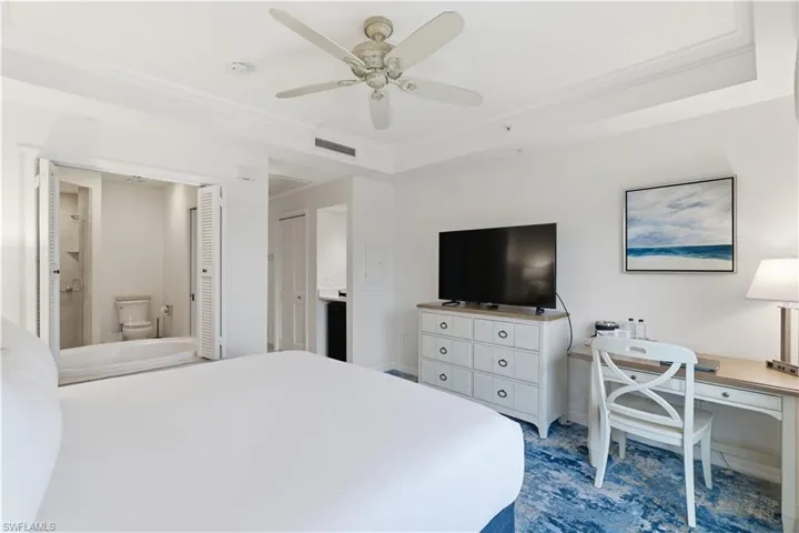 Bedroom featuring ensuite bathroom, ornamental molding, a desk, ceiling fan, and a tray ceiling