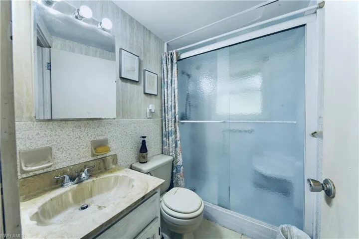 Bathroom with a shower stall, vanity, and wallpapered walls