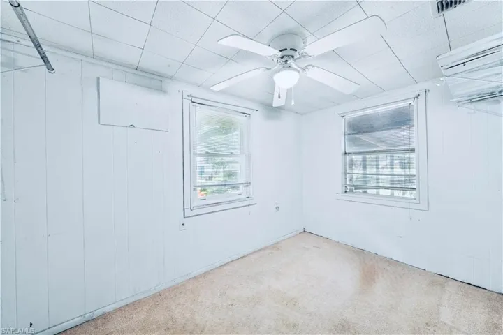Carpeted empty room featuring a ceiling fan and wood walls