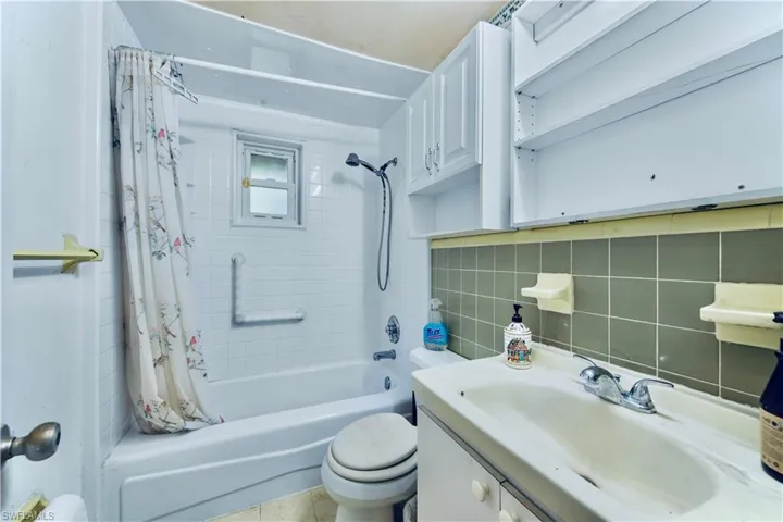 Full bathroom with shower / bathtub combination with curtain, backsplash, vanity, and tile walls