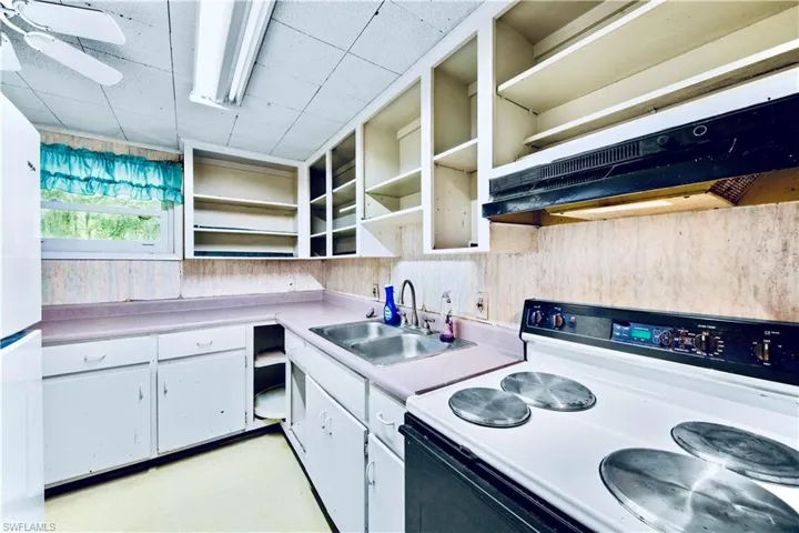 Kitchen with open shelves, white appliances, light countertops, range hood, and concrete flooring