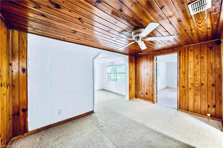 Carpeted spare room with wooden ceiling, wooden walls, and ceiling fan