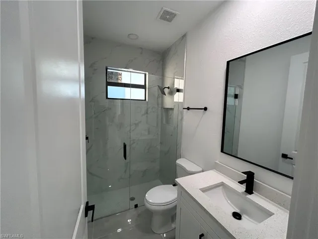 Bathroom featuring tile patterned flooring, vanity, toilet, and walk in shower