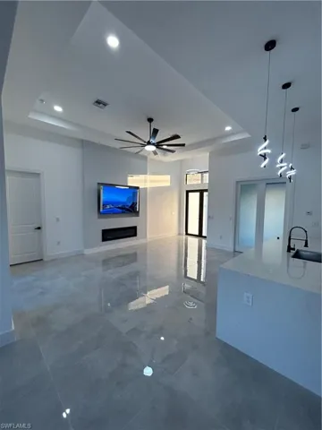 Unfurnished living room with a tray ceiling, ceiling fan, and sink