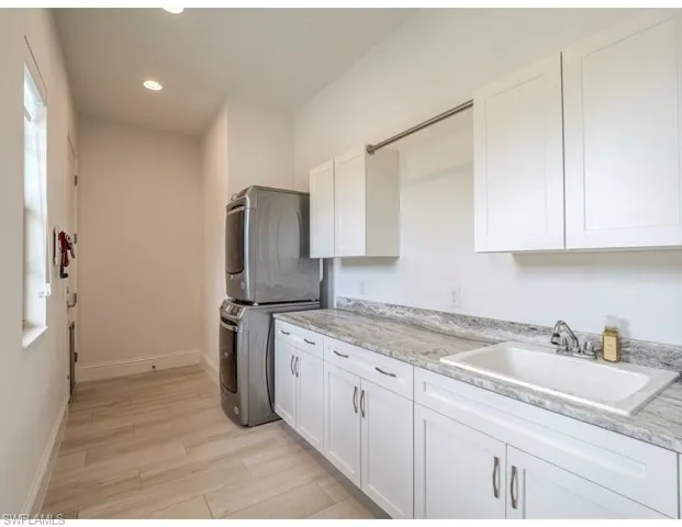 Laundry room with stacked washer / dryer, light wood-style floors, cabinet space, and recessed lighting