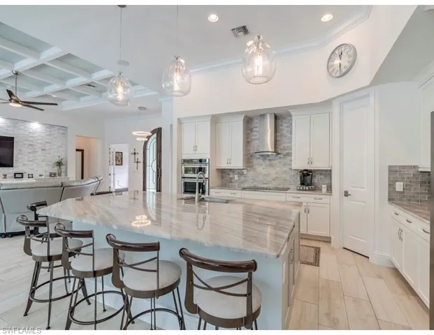 Kitchen featuring coffered ceiling, light stone counters, hanging light fixtures, a large island, and white cabinetry