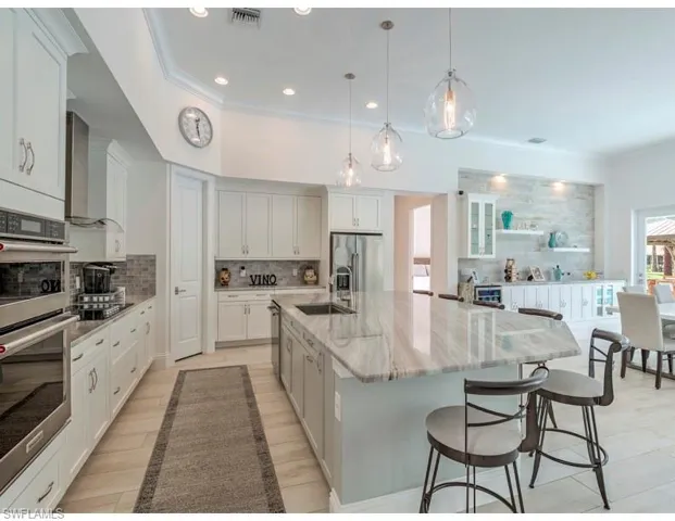 Kitchen featuring appliances with stainless steel finishes, crown molding, a large island with sink, white cabinets, and light stone countertops