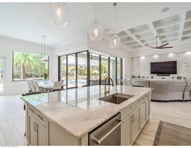Kitchen featuring light stone countertops, open floor plan, a kitchen island with sink, decorative light fixtures, and coffered ceiling