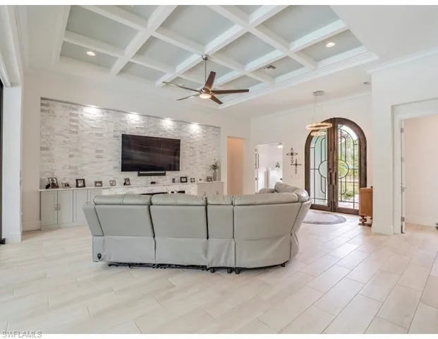 Living area with coffered ceiling, a ceiling fan, wood finish floors, beamed ceiling, and ornamental molding