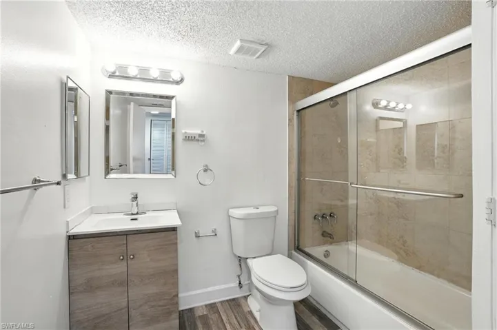 Full bath with a textured ceiling, vanity, wood finished floors, and bath / shower combo with glass door