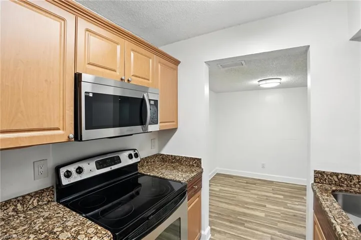 Kitchen with appliances with stainless steel finishes, a textured ceiling, light wood-style floors, dark stone countertops, and light brown cabinetry