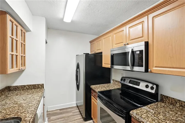 Kitchen featuring stainless steel appliances, light wood-style floors, light brown cabinets, a textured ceiling, and glass insert cabinets
