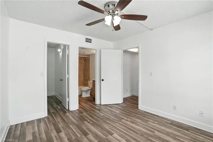 Unfurnished bedroom with wood finished floors, connected bathroom, a textured ceiling, ceiling fan, and a spacious closet