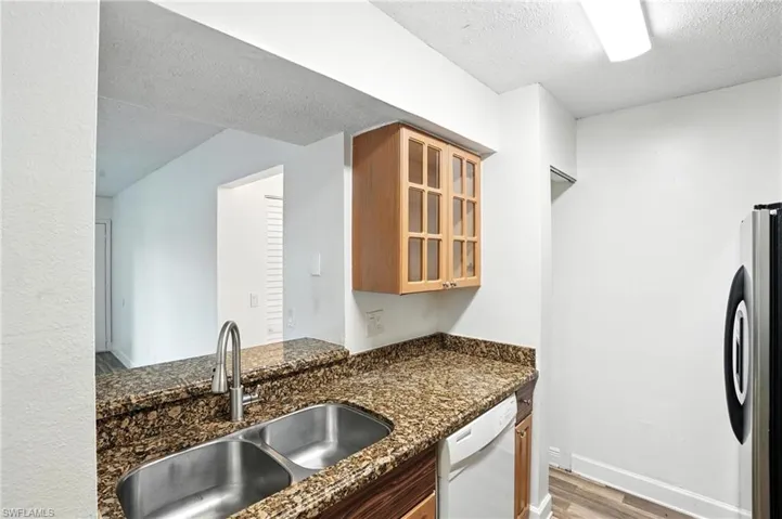 Kitchen featuring dishwasher, freestanding refrigerator, light wood-type flooring, a textured ceiling, and glass insert cabinets