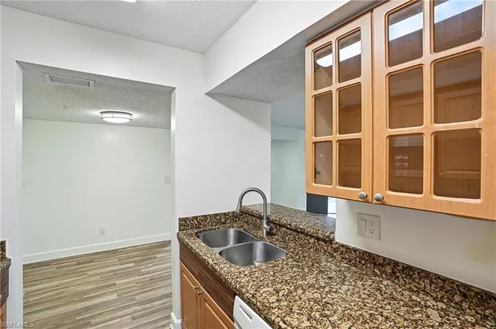 Kitchen with a textured ceiling, light wood-style flooring, glass insert cabinets, and dark stone counters
