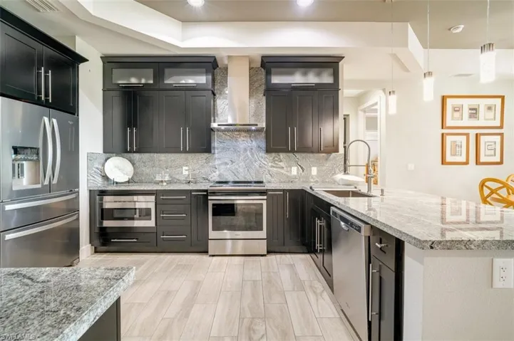 Kitchen featuring sink, hanging light fixtures, wall chimney exhaust hood, decorative backsplash, and stainless steel applces