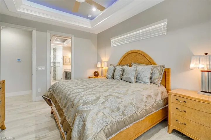 Bedroom with a tray ceiling, ensuite bath, ceiling fan, and crown molding