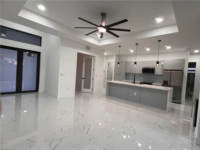 Kitchen featuring tasteful backsplash, decorative light fixtures, a tray ceiling, gray cabinets, and appliances with stainless steel finishes