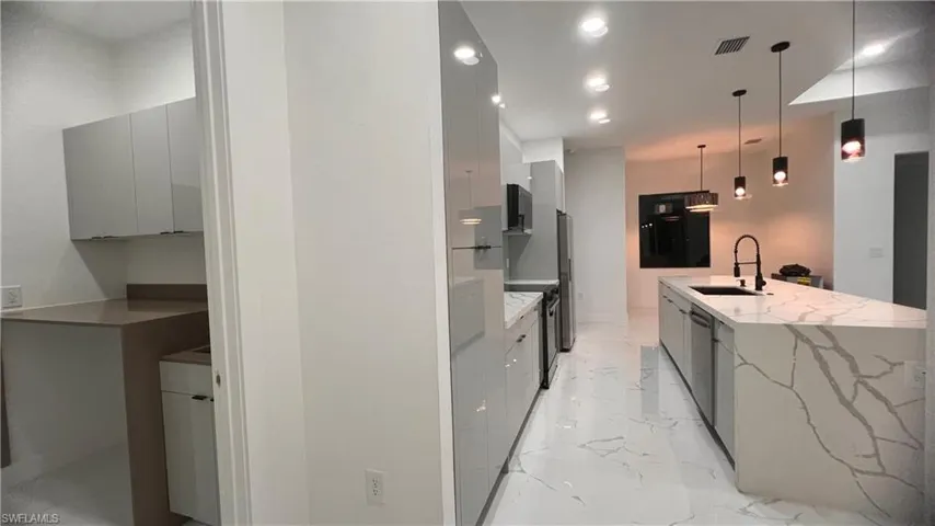 Kitchen with light stone counters, sink, and decorative light fixtures