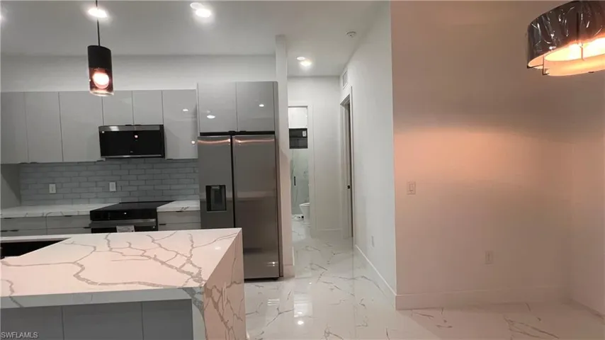 Kitchen featuring light stone countertops, white cabinetry, hanging light fixtures, backsplash, and appliances with stainless steel finishes