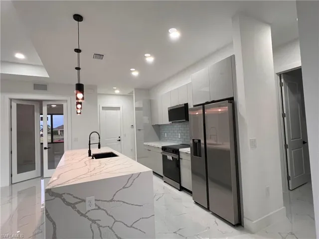 Kitchen with sink, hanging light fixtures, backsplash, an island with sink, and appliances with stainless steel finishes