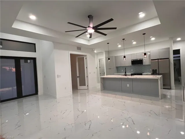Kitchen featuring decorative light fixtures, a tray ceiling, gray cabinets, decorative backsplash, and appliances with stainless steel finishes