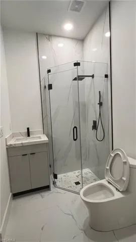 Bathroom featuring walk in shower, vanity, and toilet
