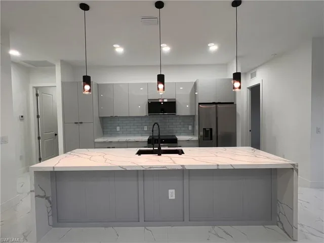 Kitchen featuring pendant lighting, backsplash, sink, light stone countertops, and appliances with stainless steel finishes