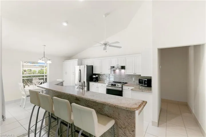 kitchen has granite counters, stainless appliances, white cabinetry