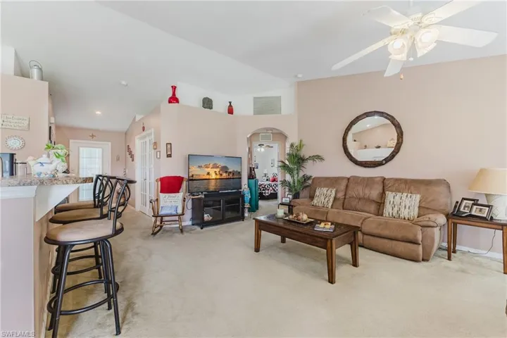 Living room featuring arched walkways, light carpet, ceiling fan, and baseboards