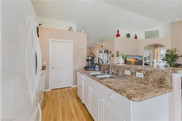 Kitchen with white appliances, a sink, white cabinets, light wood-type flooring, and arched walkways