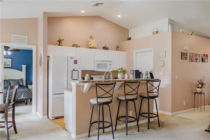 Kitchen featuring white appliances, light carpet, a kitchen bar, high vaulted ceiling, and white cabinets