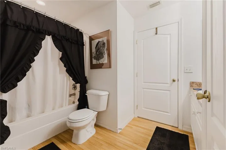 Bathroom with wood finished floors, toilet, shower / tub combo, and baseboards