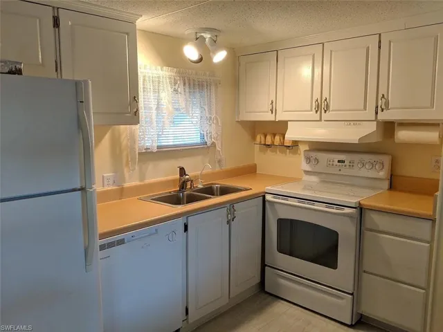Kitchen with white appliances, light countertops, white cabinetry, and a textured ceiling