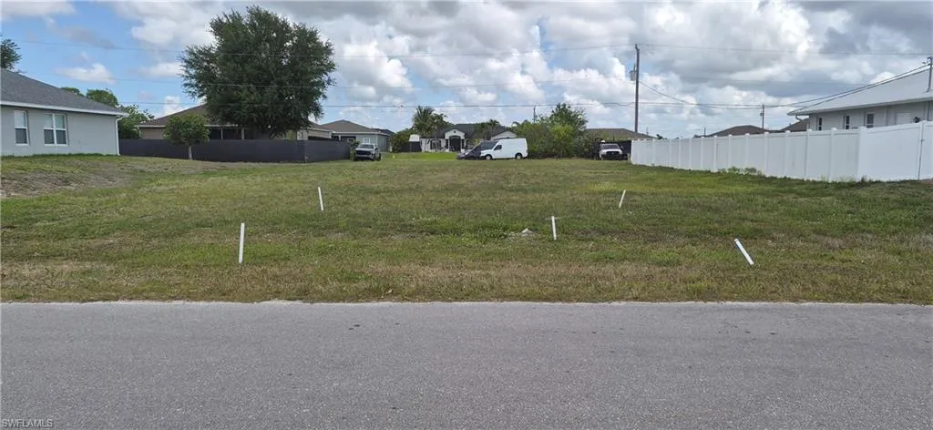Generous grass lot featuring a paved road frontage, established residential surroundings, and a white privacy fence bordering the right property line