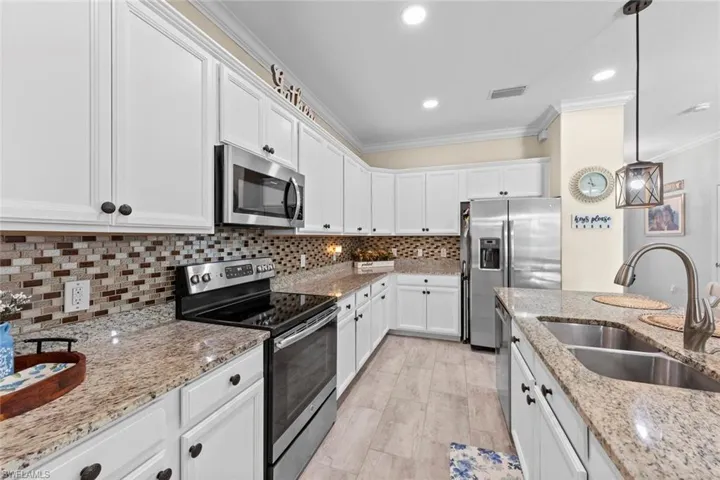 Kitchen with light stone countertops, stainless steel appliances, sink, pendant lighting, and white cabinetry