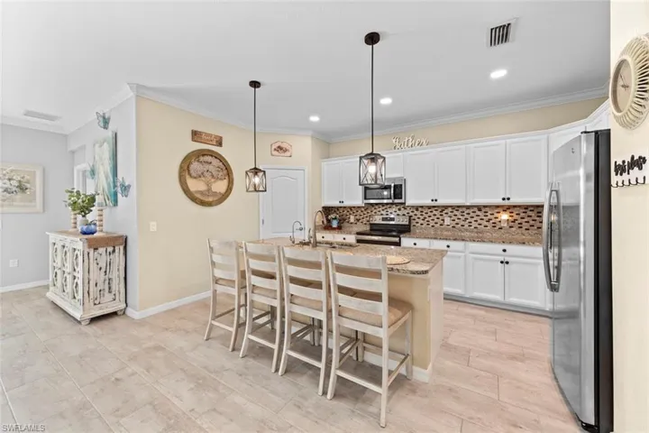 Kitchen featuring stainless steel appliances, white cabinets, a center island with sink, a kitchen bar, and decorative light fixtures
